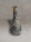 Roman blown glass made of pale glass. Small piriform body with a cylindrical neck terminating in an everted rim. Colorless glass with a fully layer of...