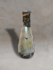 An ancient Roman translucent-glass unguentarium. It has a pyriform body, with a cylindrical neck tapering at the base, and a bent and everted rim. The...