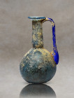 Roman bottle of iridescent light blue blown glass with spout and single handle. The handle is deep blue. It has iridescence and parts with earthy trac...
