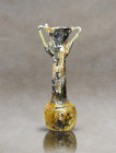 Roman cosmetic container, blown in deep green glass. It has a slender pyriform body resting on a solid flat base. Two handles have been applied to the...