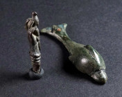 TWO ROMAN BRONZE FIGURAL ORNAMENTS Circa 2nd-3rd century AD. An applique in the shape of a dolphin; and the terminal from a cloth- or hairpin in the s...