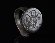 A BYZANTINE BRONZE RING DEPICTING A BIRD Circa 12th-14th century AD. With an offset round bezel showing a bird with open wings. Ring size 56 (EU)

E...