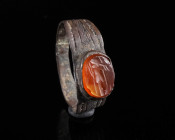 A ROMAN SILVER RING WITH A CARNELIAN INTAGLIO Circa 2nd-3rd century AD. The shoulders with incised and punched decoration; the oval intaglio showing a...