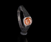 A ROMAN SILVER RING WITH A CARNELIAN INTAGLIO Circa 3rd century AD. With offset, facetted shoulders; the round intaglio depicting a female head left. ...