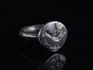 A BYZANTINE BRONZE RING DEPICTING A BIRD ON A BRANCH Circa 12th-14th century AD. With an offset shield-shaped bezel showing a bird with open wings sit...