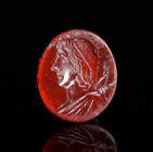 A ROMAN CARNELIAN INTAGLIO DEPICTING A BUST OF APOLLO Circa 1st-3rd century AD. Attractive and skilfully carved oval intaglio showing a draped bust of...