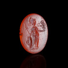 A ROMAN CARNELIAN INTAGLIO DEPICTING THE GODDESS ROMA Circa 1st-3rd century AD. Oval intaglio with the helmeted and draped goddess standing left, hold...