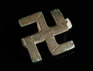 A ROMAN BRONZE SWASTIKA BROOCH Circa 2nd-3rd century AD. With four anti-clockwise rotation arms; decorated with incised grooves and lines. Pin missing...