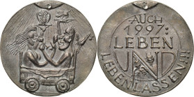 Güttler, Peter Götz *1939 Weißmetallgussmedaille 1996. Zum neuen Jahr 1997. Nacktes zuprostendes Paar einander gegenüber sitzend, halten je ein Tablet...