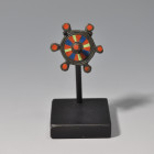 ARQUEOLOGÍA. PUEBLOS GERMÁNICOS. Fíbula con forma de escudo (ss. II-IV d.C.). Bronce. Diámetro 3 cm. Incluye peana.