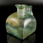 Roman Glass Jug
1st-2nd century CE
Greenish Glass, 132 mm
Jug with square body, concave base, short cylindrical neck and ledge rim with collar. Str...