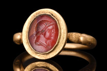 ROMAN GOLD RING WITH CARNELIAN PORTRAIT INTAGLIO 

 Ca. AD 300
 A gold finger ring featuring a rounded hoop with duck-head finials. The bezel is se...