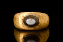 ROMAN GOLD RING WITH BANDED AGATE

 Ca. AD 100-300
 A gold finger ring composed of a rounded hoop and expanding shoulders. The oval bezel is set wi...