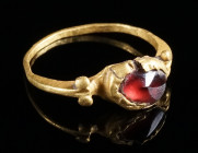 A DELICATE ROMAN GOLD RING WITH GARNET Circa 2nd-3rd century AD. The circular bezel set with a conical garnet; two pellets on each shoulder. Slightly ...