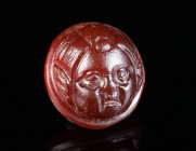 A ROMAN CARNELIAN CAMEO WITH A HEAD OF EROS Circa 1st-3rd century AD. Circular cameo carved in high relief with a frontal head of Eros, characterised ...