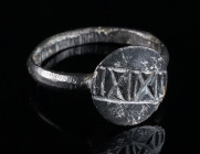 A LATE ANTIQUE/ BYZANTINE BRONZE RING WITH GEOMETRIC DESIGN Circa 5th-8th century AD. With a projecting round bezel engraved with ‘IIXIXII’. Ring size...