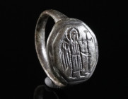 A BYZANTINE BRONZE RING WITH AN ANGEL Circa 12th-14th century AD. Ring with octagonal bezel depicting an angel with halo standing right, holding a cro...