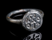 AN EARLY BYZANTINE BRONZE RING WITH INSCRIPTION AND CROSS Circa 6th-7th century AD. Bronze ring with offset round bezel depicting a cross surrounded b...