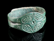 A THIN HAMMERED MEDIEVAL BRONZE RING Circa 10th-12th century AD. With a split hoop with overlapping ends; the oval bezel decorated with an ornamental ...