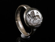 AN EARLY BYZANTINE BRONZE RING WITH A BIRD Circa 6th-7th century AD. With an offset round bezel depicting a bird with outstretched wings, a branch in ...