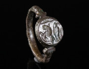 A LATE ROMAN BONZE RING WITH LION AND EAGLE Circa 4th century AD. Ring with raised circular bezel depicting a stylised lion and an eagle. The hoop is ...