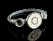 A DELICATE ROMAN BRONZE RING WITH ENAMEL Circa 2nd century AD. Ring with an offset circular, enamelled bezel. Two roundels on the shoulders, on either...