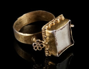 AN EARLY MODERN SILVER-GILT RING WITH STONE Circa 16th century AD. The projecting square bezel set with a crystal or glass stone. Granulated decoratio...