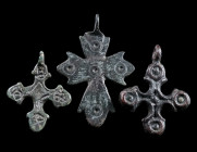 A GROUP OF THREE BYZANTINE BRONZE CROSS PENDANTS Circa 6th-12th century AD. Three small decorated cross pendants. One with five punched ring-and-dot m...