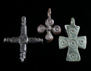 A GROUP OF THREE BYZANTINE BRONZE CROSS PENDANTS Circa 6th-12th century AD. Three small decorated cross pendants. One with five punched ring-and-dot m...