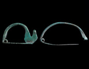 TWO GREEK-TYPE BOW BROOCHES Circa 6th-5th century BC. Both with ribbed bow. With spiral and pin. Catch plate of the smaller brooch slightly damaged. L...