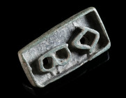 A BYZANTINE BRONZE BREAD STAMP Circa 5th-8th century AD. Rectangular in form, with an abbreviated Greek inscription and a small strap loop/handle at t...