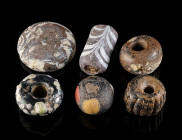 A GROUP OF FIVE ANCIENT GLASS BEADS AND A GAMING PIECE Circa 6th century BC - 1st century AD. Three ‘black’ glass beads with coloured ‘dots’ (glass fr...