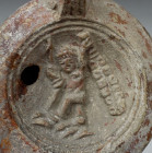 Roman oil lamp depicting a winged genie brandishing Hercules club and makers mark, Type Bussière D II 1