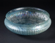 A ROMAN PALE BLUE-GREEN GLASS FINELY RIBBED BOWL
Circa early 1st century AD.
An exquisite shallow mould-blown glass bowl with fine vertical ribs ext...