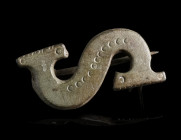 A ROMAN BRONZE S-SHAPED BROOCH
Circa 2nd-3rd century AD.
S-shaped plate brooch decorated with punched rings/crescents. Ends with notched edges. With...