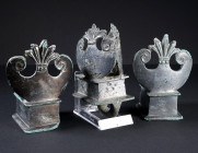 A SET OF THREE ROMAN TINNED BRONZE CHARIOT FITTINGS
Circa 2nd-3rd century AD.
a) Two terminal mounts with cuboid base and flared rim, surmounted by ...