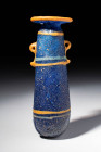 PHOENICIAN PYRIFORM COLOURED GLASS UNGUENTARIUM

 Ca. 600 - 400 BC A translucent light blue glass unguentarium, with opaque yellow handles and rim-d...