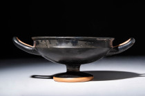 GREEK BLACK GLAZED KYLIX WITH STANDING BASE 

 Ca. 480 - 450 BC A Greek black glazed kylix, a twin-handled cup with a concave, offset lip and shallo...