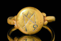 MEROVINGIAN GOLD RING WITH MONOGRAM

 Ca. AD 500 - 700 A stunning Merovingian gold ring with a slender hoop. The bezel is connected with two gold pe...