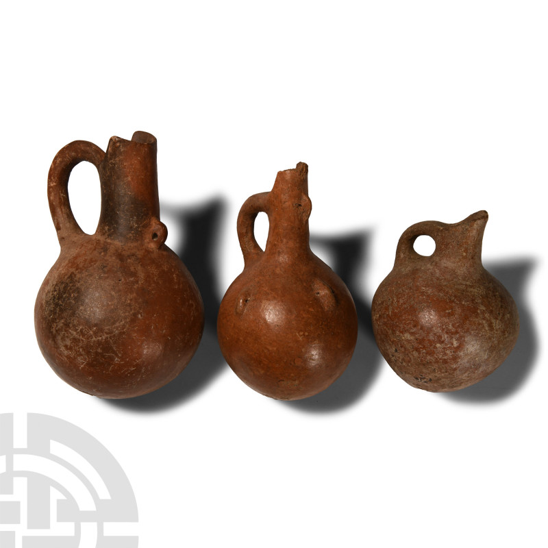 Circa 1400-600 B.C.. Group of three spherical jugs each with a tall neck and lat...