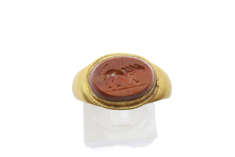 A gold finger ring with central ellipsoid cell and inset carnelian cabochon inta...