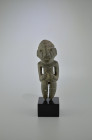 Mezcala, 300 - 100 BC. H 19.5cm. Gray stone figure of a standing human with big head with schematic features, dressed with a cap. The short legs are d...