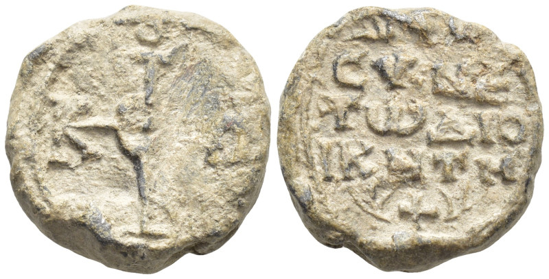 Byzantine Lead Seal, (18mm, 11.3 g) Cruciform monogram. / Legends in four lines.