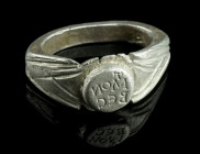 A ROMAN SILVER RING WITH INSCRIPTION
Circa 3rd century AD.
Ring with flared and angled shoulders and a projecting round bezel. The shoulders and the h...