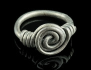 A ROMANO-CELTIC SILVER RING WITH SPIRAL
Circa 1st century AD.
With a large central spiral and overlapping ends secured with two spiral twists. 
Ring s...
