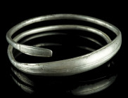 AN EASTERN CELTIC SILVER BRACELET
Circa 2nd-1st century BC.
Solid spiral bracelet with widened convex mid-section and flattened ends. Incised linear d...