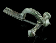 A LATE ROMAN BRONZE CROSSBOW BROOCH
Circa 4th century AD.
With arched bow and onion-shaped terminals ('Zwiebelknöpfe'). Decorated with two deep groove...