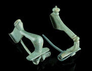 TWO ROMAN BRONZE BROOCHES
Circa 2nd-3rd century AD.
A knee brooch, and a strongly profiled brooch. Both with spring and pin. Spring of the knee brooch...