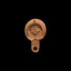 Roman Oil Lamp with Actor's Mask
1st-2nd century AD. A terracotta oil lamp with broad chamfered shoulder and three pierced lugs, recessed discus with...