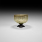 Byzantine Glass Footed Cup with Designs
6th-8th century AD. An aqua glass bowl with rolled rim and panels with geometric motifs, dark blue pedestal f...